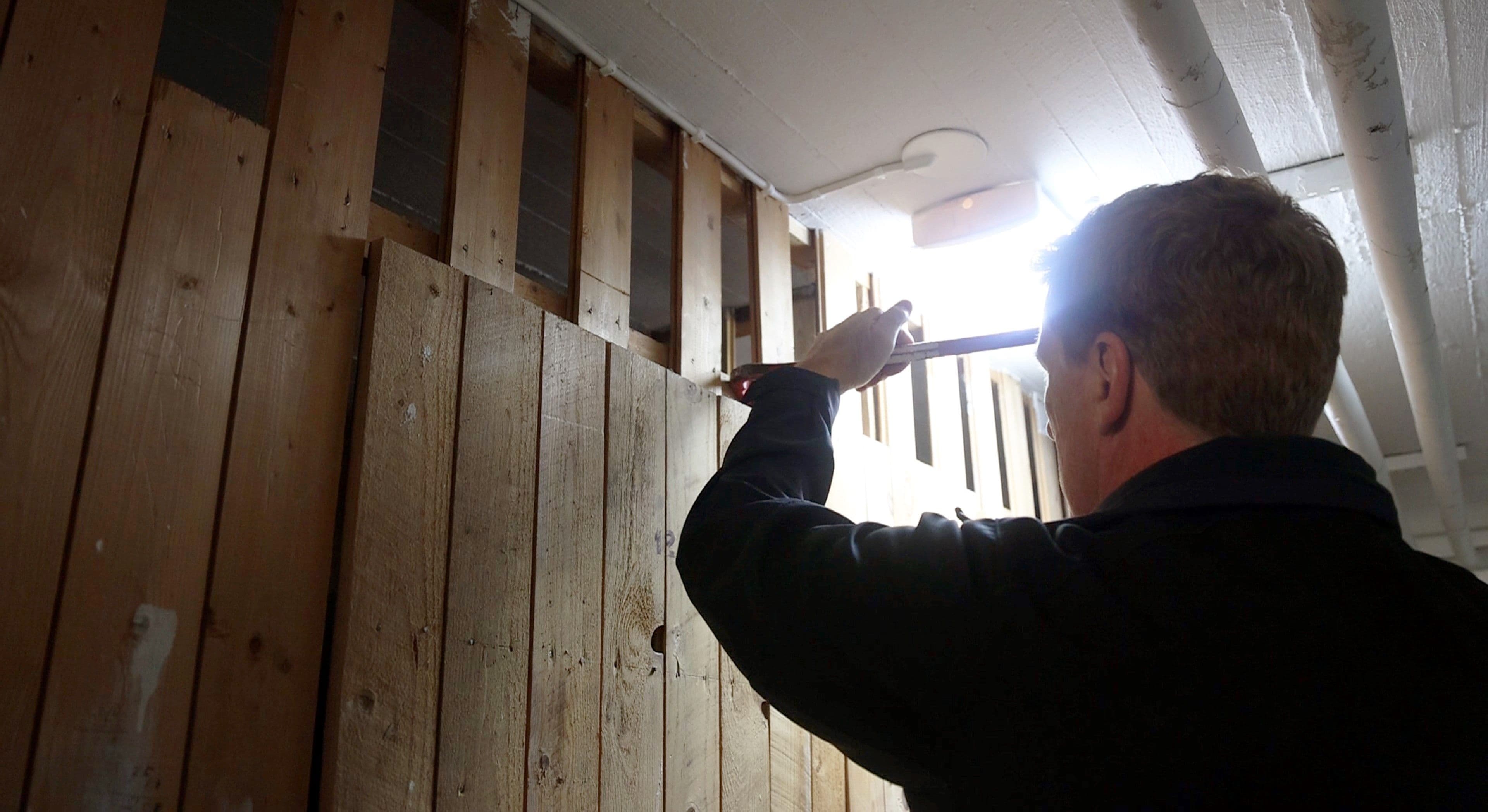 Tekniker som tar bort en träväggssektion i ett skyddsrum för att frigöra utrymme och säkerställa korrekt funktion.